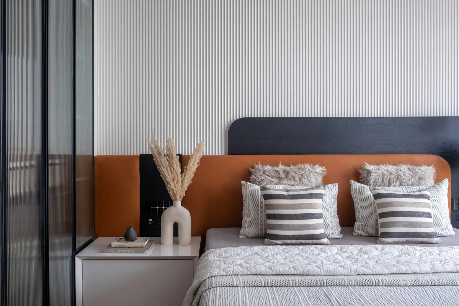Step into one of the house in India Bulls Blu with a serene and stylish bedroom oasis, featuring a beautiful light brown accented bed, cozy furry cushions, and a bold stripe patterned accent wall design | AVN Interiors
